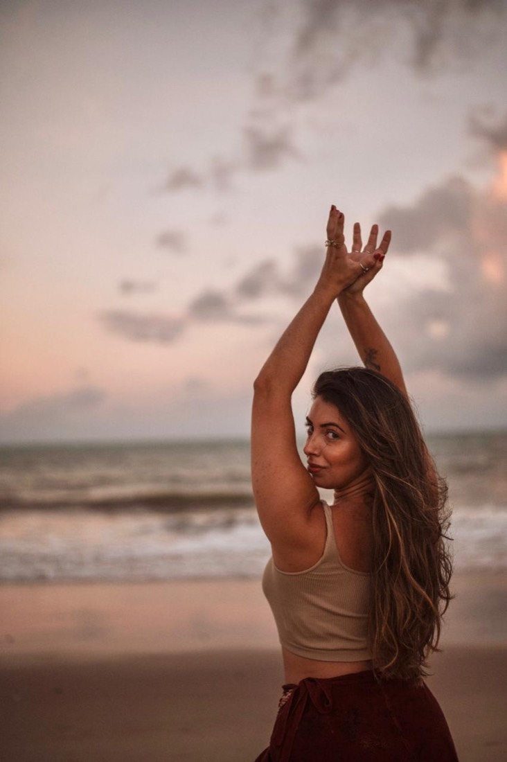 Madu de braços erguidos ao pôr do sol na praia